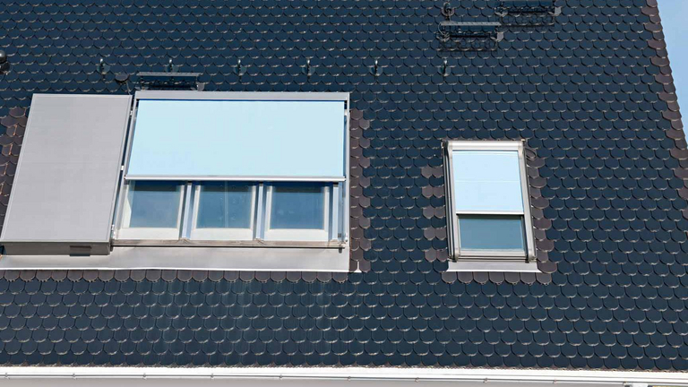 Ein Panorama Dachfenster Azuro ist mit einem weiteren Dachfenster in einem Dach mit schwarzen Ziegeln verbaut